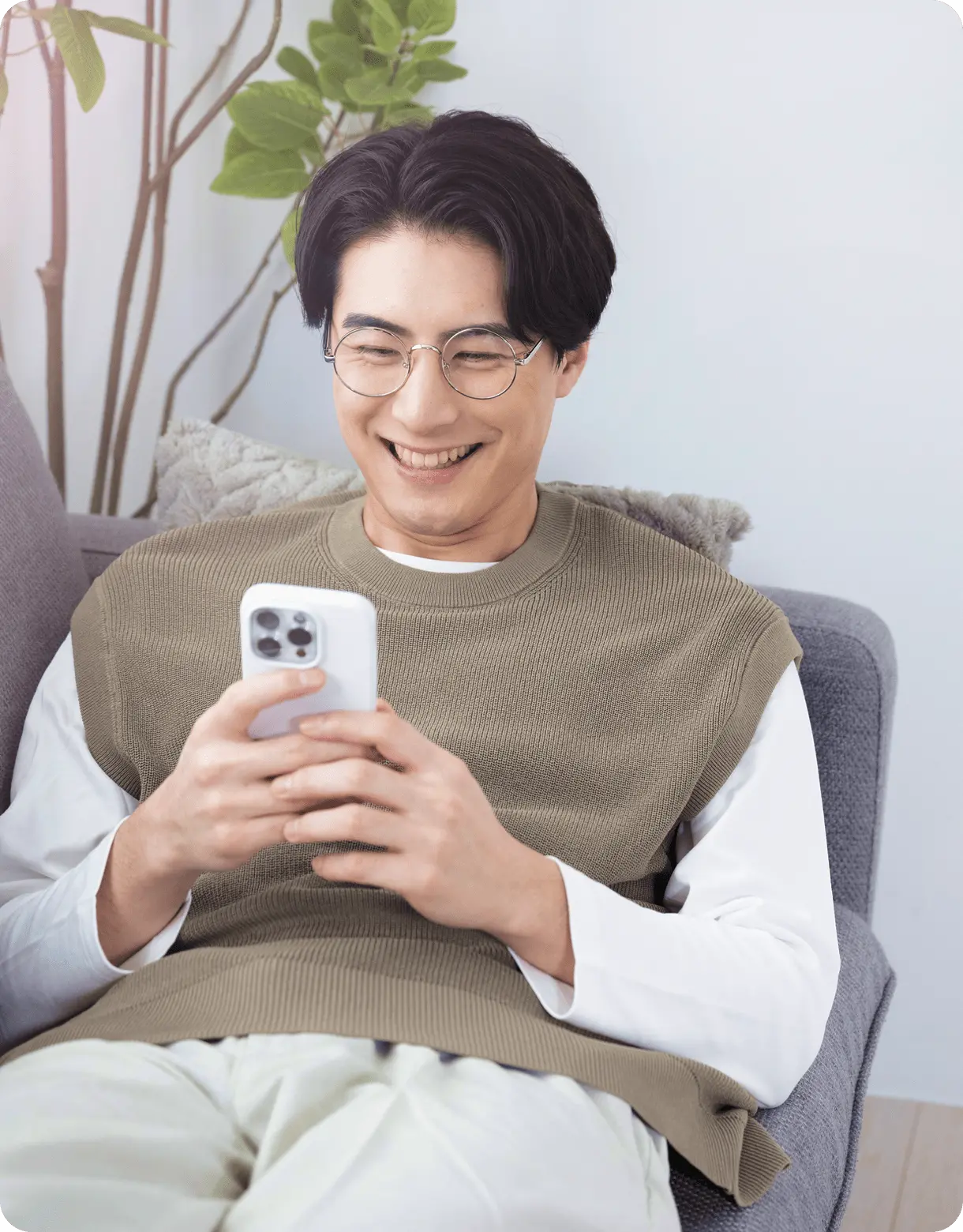 ソファに座りながらスマートフォンを操作し、笑顔を見せる若い男性