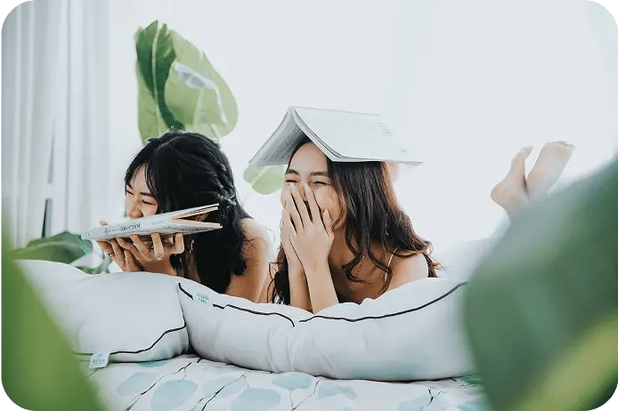ベッドの上で本を読んで笑い合う、仲の良い2人の女性の楽しげな様子
